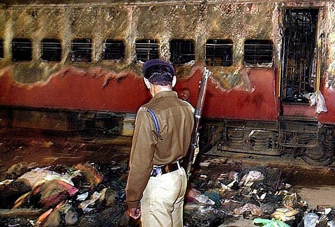 A policeman looks over a burnt coach and belongings of Hindu activists at Godhra station, on 28 February 2002. (File Photo | AFP)