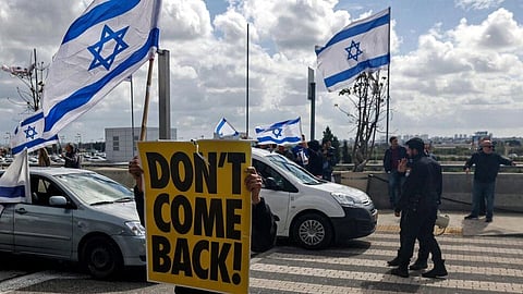 A demonstrator holds an Israeli flag and a sign reading in English 'don't come back!', referring to Prime Minister Benjamin Netanyahu who heads to Germany on an official visit. (Photo | AFP)