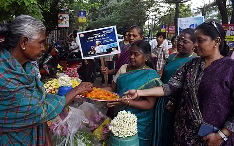 DMK women wing members distribute sweets to the public after the announcement of monthly honorarium of rupee 1000 to to family heads of women, at Gandhipuram in Coimbatore. (Photo | S Senbagapandiyan)