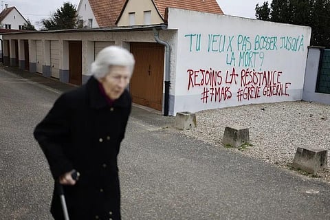 An elderly woman walks past graffitis reading 'You want to work until death? Join resistance, General Strike on March 7' in Strasbourg eastern France, Sunday, March 5, 2023. (Photo | AP)