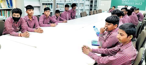 A group of students sitting in a library seem to ill at ease rather than making use of the resources at their disposal