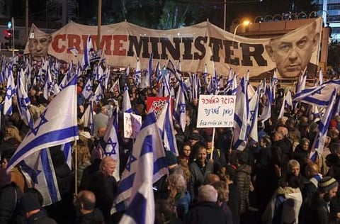 Demonstrators wave flags next to a banner depicting Israeli Prime Minister Benjamin Netanyahu during a rally to protest the government's judicial overhaul bill. (Photo | AFP)