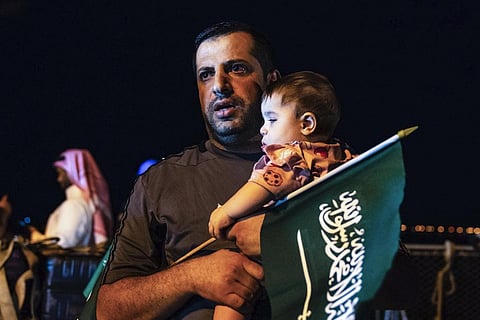 An evacuee holds a child and a Saudi flag as they arrive at Jeddah Port on Monday, April 24, 2023, after being evacuated from Sudan to escape the conflict. (Photo | AP)