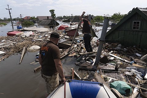 Animal rescuers make their way through floating debris to rescue a dog in the flooded area after the dam collapse in Kherson, Ukraine. (Photo | AP)