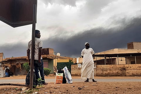 Smoke rises above buildings as people wait on the side of a road with some belongings, in Khartoum on June 10, 2023. (Photo|AFP)