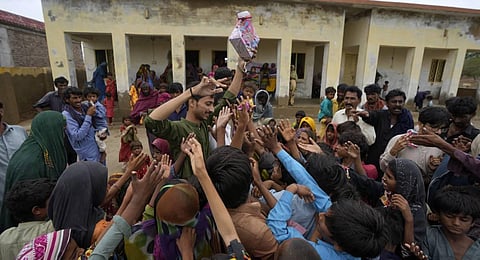 A volunteer distributes food items among children at a camp set up for internally displaced people from coastal areas due to Cyclone Biparjoy, in Badin, Pakistan's Sindh province. (Photo | PTI)