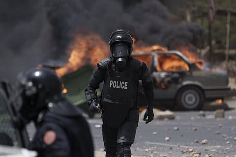 A riot police officer runs past a burning car during a protest at the Cheikh Anta Diop University campus in Dakar, Senegal. (Photo | AP)