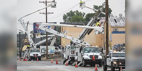 Line workers in boom trucks and on the street work to replace broken utility poles and lines as rain moves in on Peoria Avenue over the Broken Arrow Expressway on June 21, 2023, in Tulsa | AP