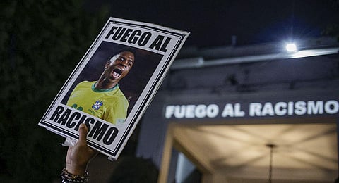 A protester holds up a photo of Brazilian soccer star Vinicius Jr and a message that reads in Portuguese; 'Fight racism' (Photo | AP)