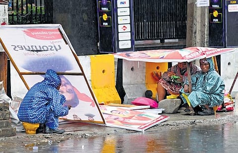 Amid rains in the city, daily wage labourers take shelter under an advertisement banner in Ameerpet on Wednesday. (Photo | Vinay Madapu)