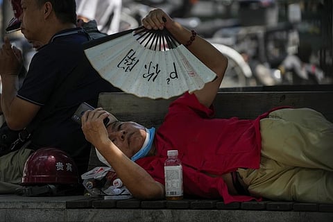 FILE - A man cools himself with a fan while browsing his phone on a sweltering day in Beijing, July 16, 2023. (Photo | AP)