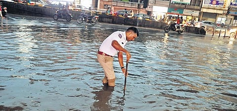 A traffic  cop  tries to clear a blocked manhole near the Prakash Nagar Metro Station following a heavy rain  in Hyderabad on Monday evening /| Sri Loganathan Velmurugan
