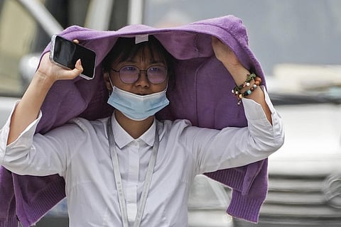 A woman uses a sweater to shield from the sun as she walks on a street on a hot day in Beijing, July 3, 2023. (Photo | AP)