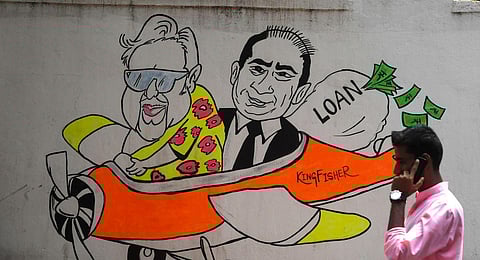 FILE - In this photo taken on April 2, 2019, a commuter walks past a wall graffiti displaying cartoons of Indian businessmen turned fugitives Vijay Mallya and Nirav Modi. (Photo | AFP)