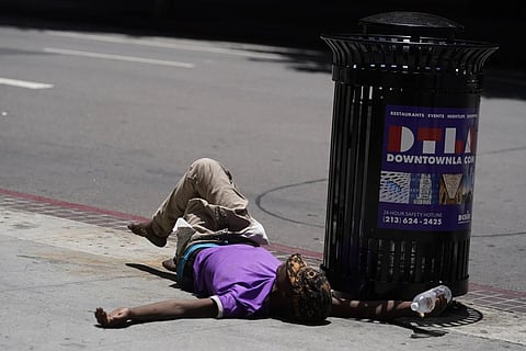 A homeless person lies on the sidewalk while holding a water bottle, July 2, 2023 in downtown Los Angeles. (Photo |AP)