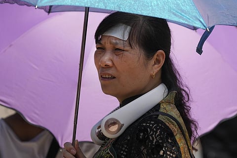 A woman wearing an electric fan, putting a cooling pad on her forehead and carrying an umbrella visits the Forbidden City on a sweltering day in Beijing. (Photo | AP)