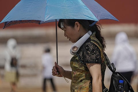 A woman wearing an electric fan and carrying an umbrella visits the Forbidden City on a sweltering day in Beijing (Photo | AP)