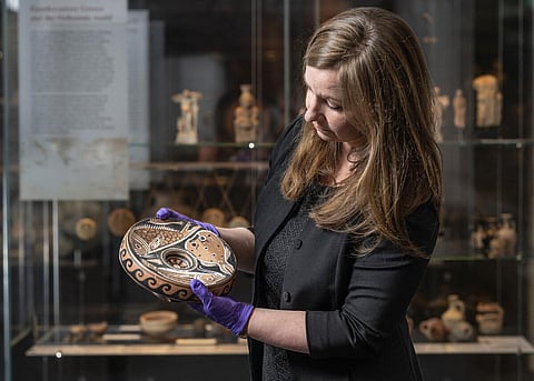 This undated handout photo made available on September 15, 2023 by the Australian National University shows ANU Museum curator Georgia Pike-Rowney holding a red Apulian fish plate. (Photo | AFP)