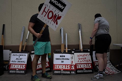 Two demonstrators pick up signs outside the Paramount Pictures Studio in Los Angeles. (Photo | AP)