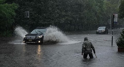 A man clears debris from a drain as a car make their way through floodwater in Brooklyn, New York. (Photo | AFP)
