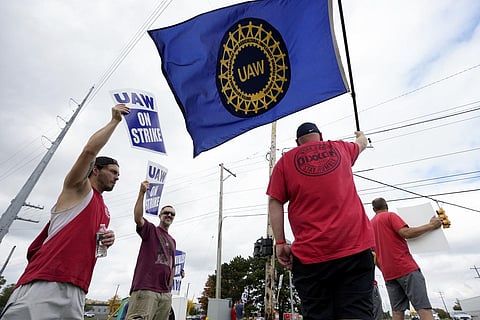 United Auto Workers members hold picket signs and a flag near a General Motors Assembly Plant in Delta Township, Mich., Friday, Sept. 29, 2023. (Photo | AP)