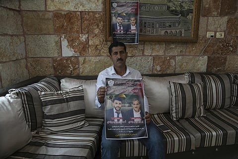 A West Bank resident holds up a poster of his brother and nephew who were killed by Israeli settlers during a funeral procession on Oct 12 in the West Bank. (AP)