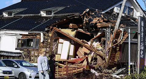 Residents walk past a damaged building in the city of Wajima, Ishikawa prefecture. (Photo | AP)