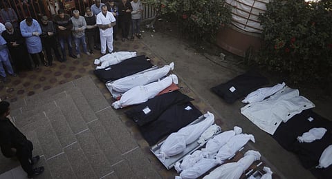 Palestinians pray near the wrapped bodies of relatives killed in the Israeli bombardment of the Gaza Strip, outside a morgue in Khan Younis. (Photo | AP)
