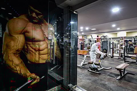 A worker wearing PPE suit sanitizes gym equipments in Delhi. (Photo | PTI)
