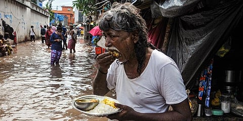 A local has a meal next to a flooded street after landfall of cyclone 'Yaas', in Kolkata. (Photo | PTI)