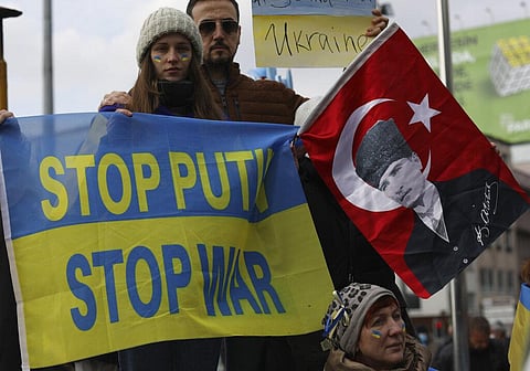 Women with their faces painted in the colors of the Ukrainian flag hold a banner and a Turkish flag with an image of Turkey's founder Mustafa Kemal Ataturk. (Photo | AP)
