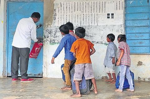 A teacher opens the lock of a school as children wait outside in a tribal village school in the Asifabad district.