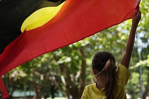 A young girl holds an Aboriginal flag at an Indigenous Australians protest  during Australia Day in Sydney, Friday, Jan 26, 2024.