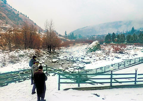 People stand at a snow covered field after light snowfall at Tangmarg. 