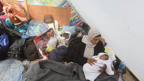 A Palestinian woman displaced by Israeli air and ground offensive on the Gaza Strip holds her baby in a tent near Kerem Shalom crossing in Rafah, Sunday, Jan. 14, 2024.