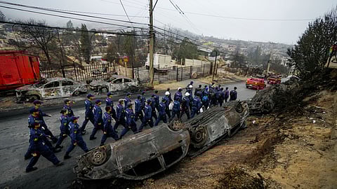 Chilean Navy personnel walk past overturned, charred cars as they deploy to help aid the Villa Independencia neighborhood affected by forest fires.