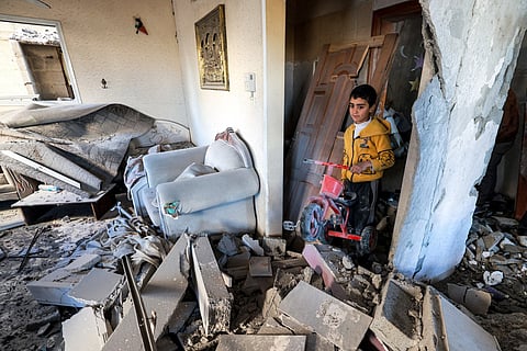 A boy holds a toy plastic tricycle while standing amidst the rubble of a destroyed home in the aftermath of Israeli bombardment on Rafah in the southern Gaza Strip.