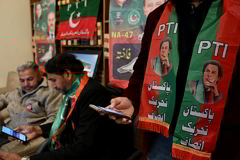 Pakistan's former prime minister Imran Khan's supporters wear scarves with prints of his Pakistan Tehreek-e-Insaf (PTI) party as they listen to a virtual election campaign on phones at Khan's PTI office in Islamabad on February 3, 2024.