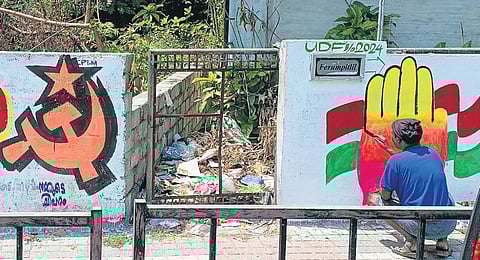 A UDF worker paints the graffiti of the Congress next to a wall displaying the LDF’s election symbol