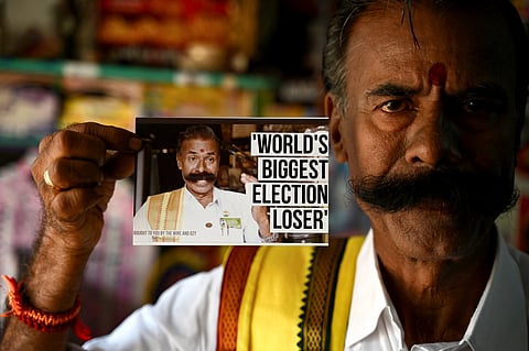 Independent candidate K. Padmarajan, a tyre repair shop owner popularly known as "Election King", shows a photograph featuring himself stating 'World's Biggest Election Loser'.