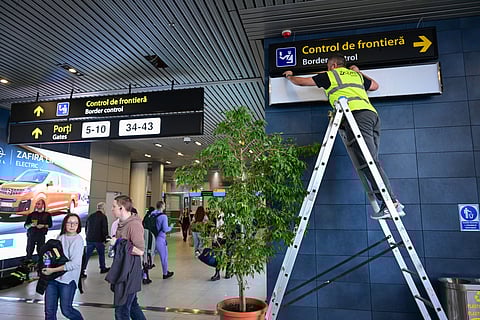 A Romanian worker changes the signs to lead passengers of the non-Schengen flights toward newly installed border control points inside the Henri Coanda International Airport in Otopeni, Romania, on March 28, 2024.