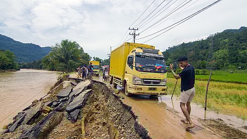A man guides a truck along an erosion-damaged road following flash flooding in Pesisir Selatan Regency, West Sumatra.
