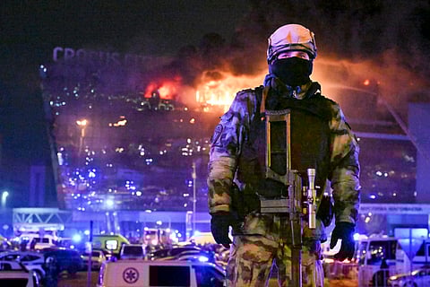 A Russian soldier secures an area as a massive blaze can be seen over a concert venue on the western edge of Moscow, Russia, Friday, March 22, 2024.