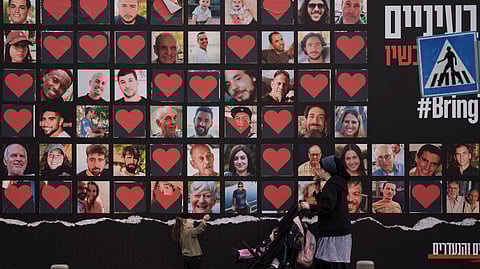 A woman and her children walk past a wall with photographs of hostages who were kidnapped during the Oct. 7 Hamas cross-border attack in Israel in Jerusalem.