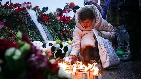 A woman lights candles at the fence next to the Crocus City Hall, on the western edge of Moscow, Russia, Saturday, March 23, 2024. 