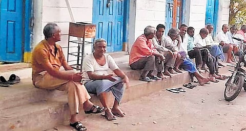 Workers are seen seated outside a closed powerloom unit in Sircilla