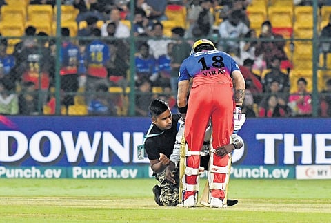 A security staffer grabs the youth, as he touches the feet of cricket icon Virat Kohli, during the RCB-Punjab Kings IPL clash, in Bengaluru on Monday