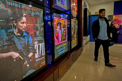 A man stands next to a poster of the movie Article 370 displayed at a cinema hall in Guwahati, India.