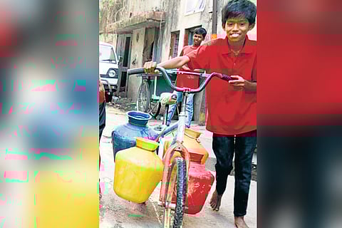 A boy carries water pots on a bicycle in Shanthinagar in Bengaluru on Wednesday