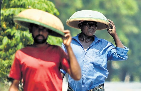 Two daily wage labourers are seen shielding themselves from the sun as they make their way back home after a day’s work in Hyderabad. 